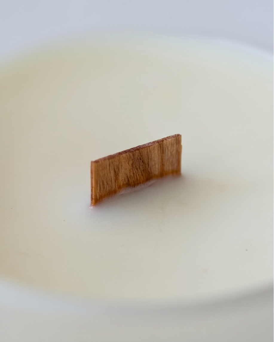 Extreme close-up of an FSC-certified wooden wick rising from a smooth ivory soy wax surface inside a The Lab soy candle by The Phoenix Candles, with shallow depth of field softening the foreground and background wax on a white surface.