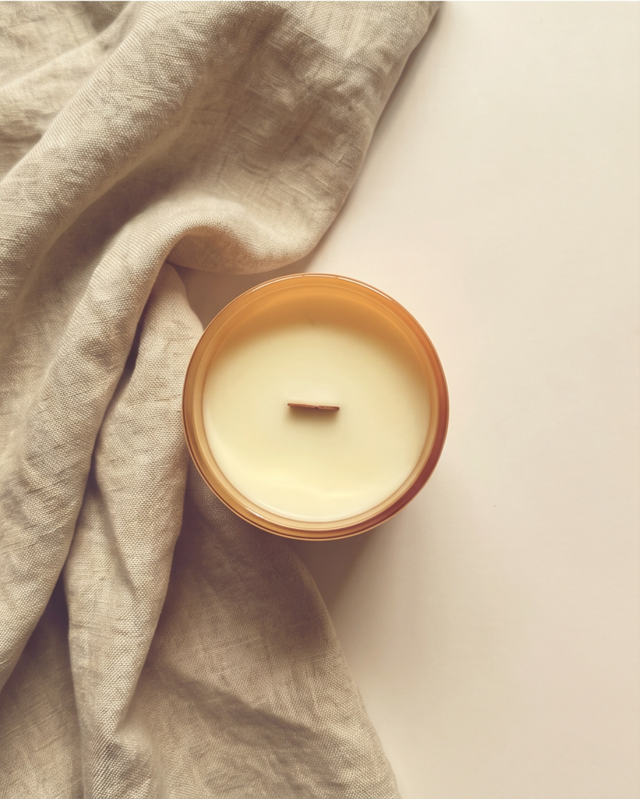 Overhead view of the Optimism crystal-infused soy candle by The Phoenix Candles, looking down into the open matte peach vessel revealing a smooth ivory soy wax pour and FSC-certified wooden wick, with a bunched natural linen cloth draped across the left side of the frame on a clean cream surface.