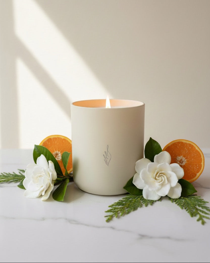 Cream candle with a logo on a white surface with flowers and oranges.