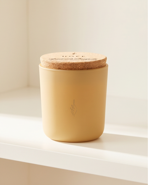 The Hope crystal-infused soy candle by The Phoenix Candles in a matte canary yellow reusable glass vessel with cork lid laser-engraved with "Hope – Infused with Amazonite, Blanc Citrus, Driftwood" and laser-engraved brand flame logo on the front, displayed on a white window ledge in soft natural light against a clean white background.